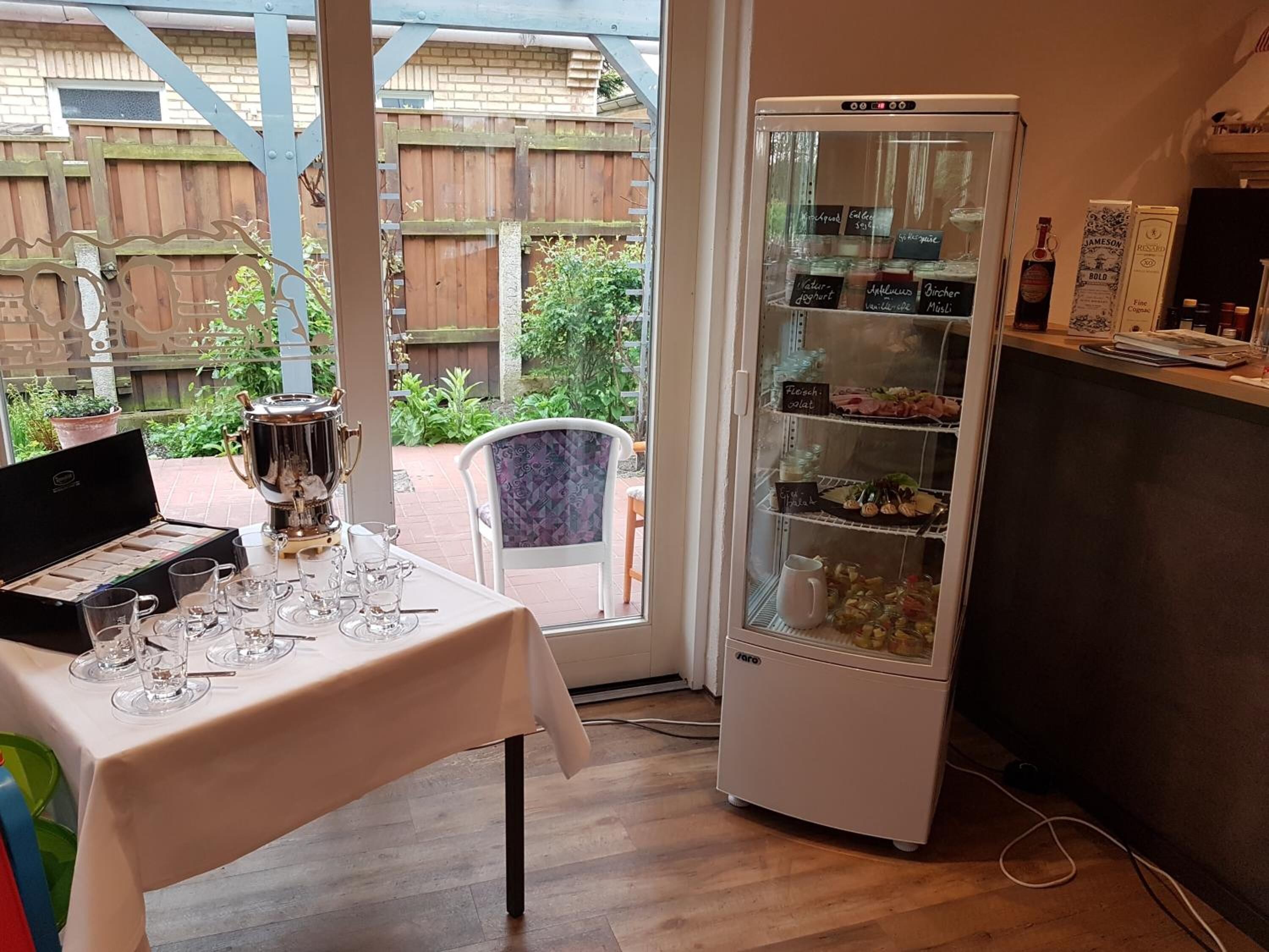 Ein Zimmer mit Esstisch, einer Speisekammer mit Lebensmitteln und Blick auf einen Holenzaun.
