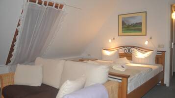 A bedroom with a bed, a sofa, a painting on the wall, and a window with curtains.