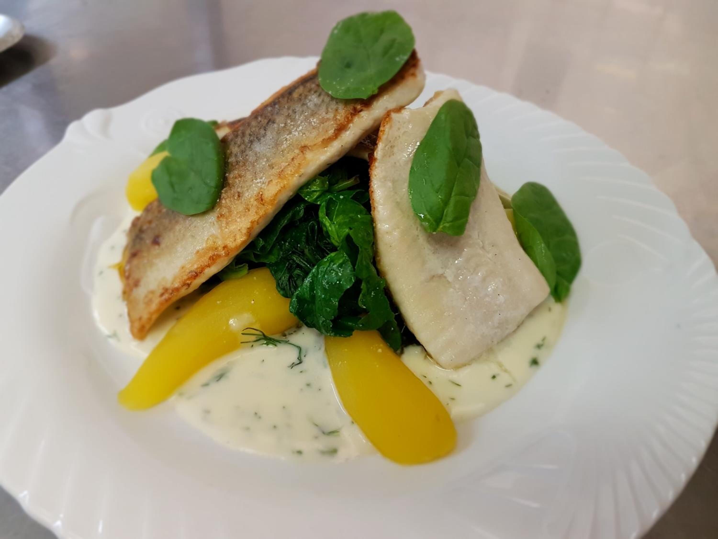 Ein weißer Teller mit Fisch, Spinat und gelbem Gemüse.