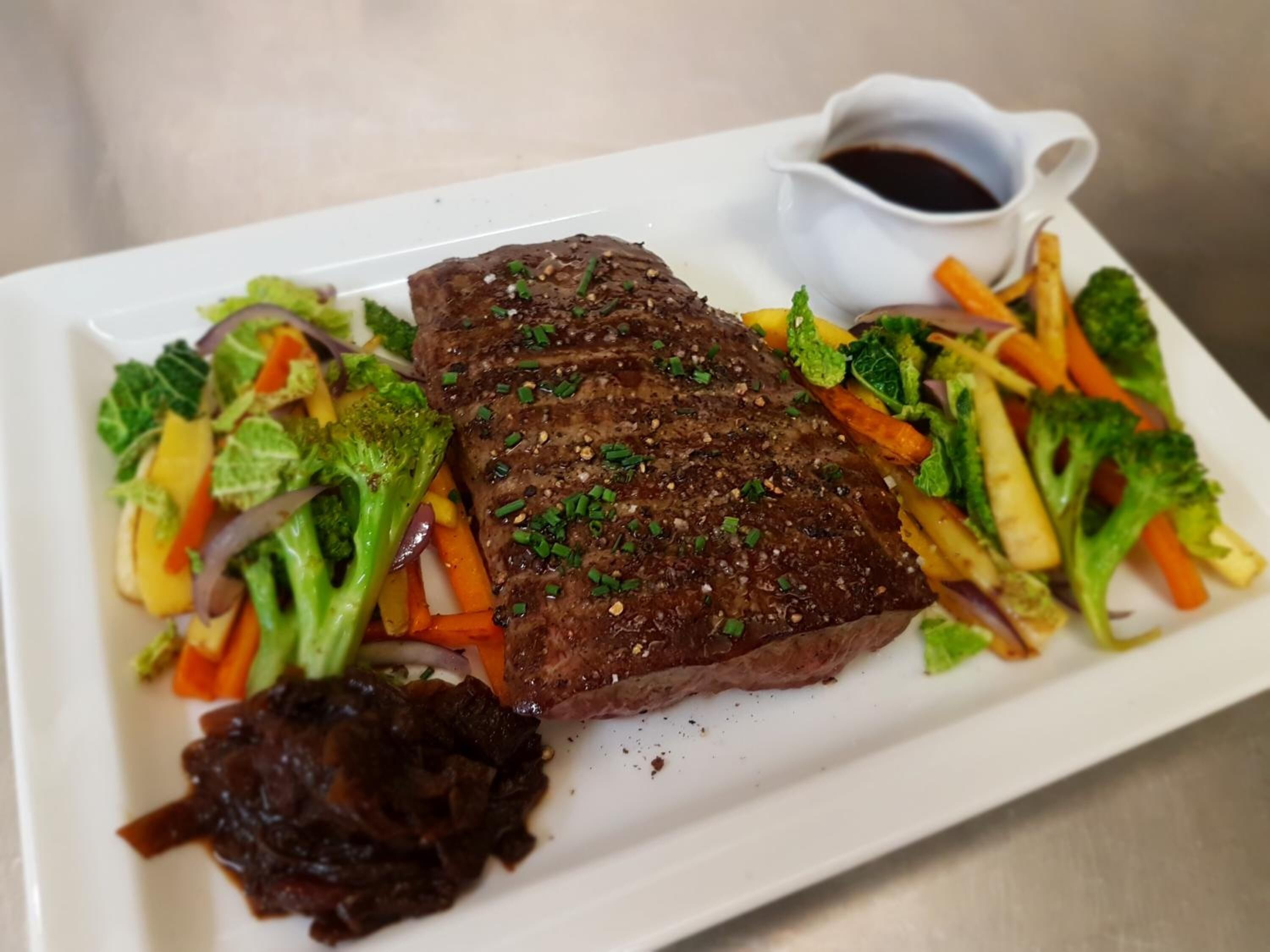 A plate with steak, vegetables, and a small bowl of sauce.