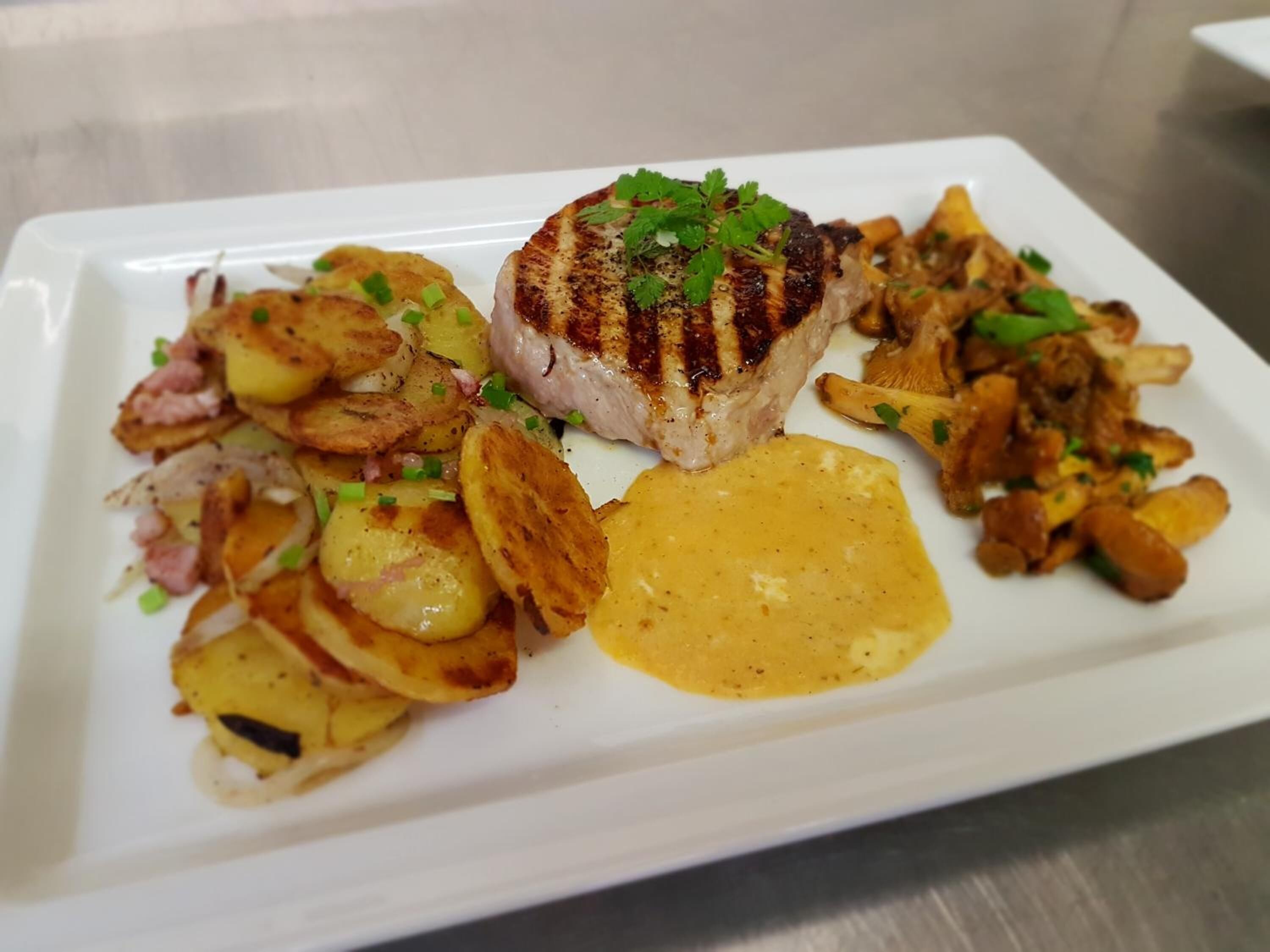 A plated meal with grilled meat, roasted potatoes, and mushrooms, served on a white rectangular plate.