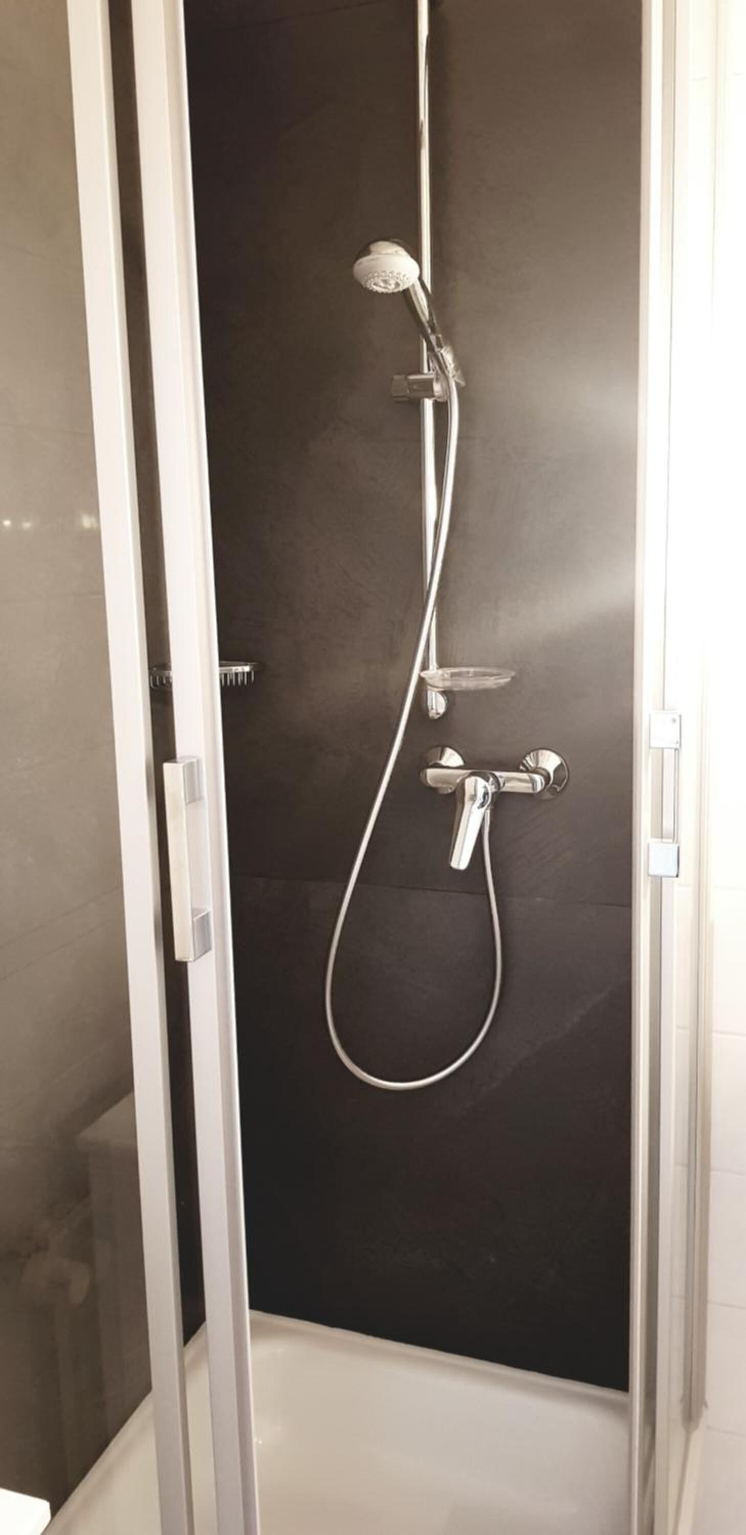 A walk-in shower with a glass door, a handheld showerhead, and a wall-mounted faucet.