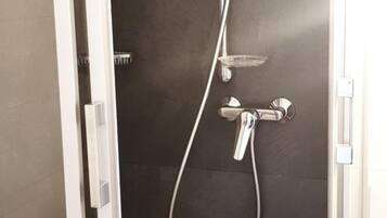 A walk-in shower with a glass door, a handheld showerhead, and a wall-mounted faucet.