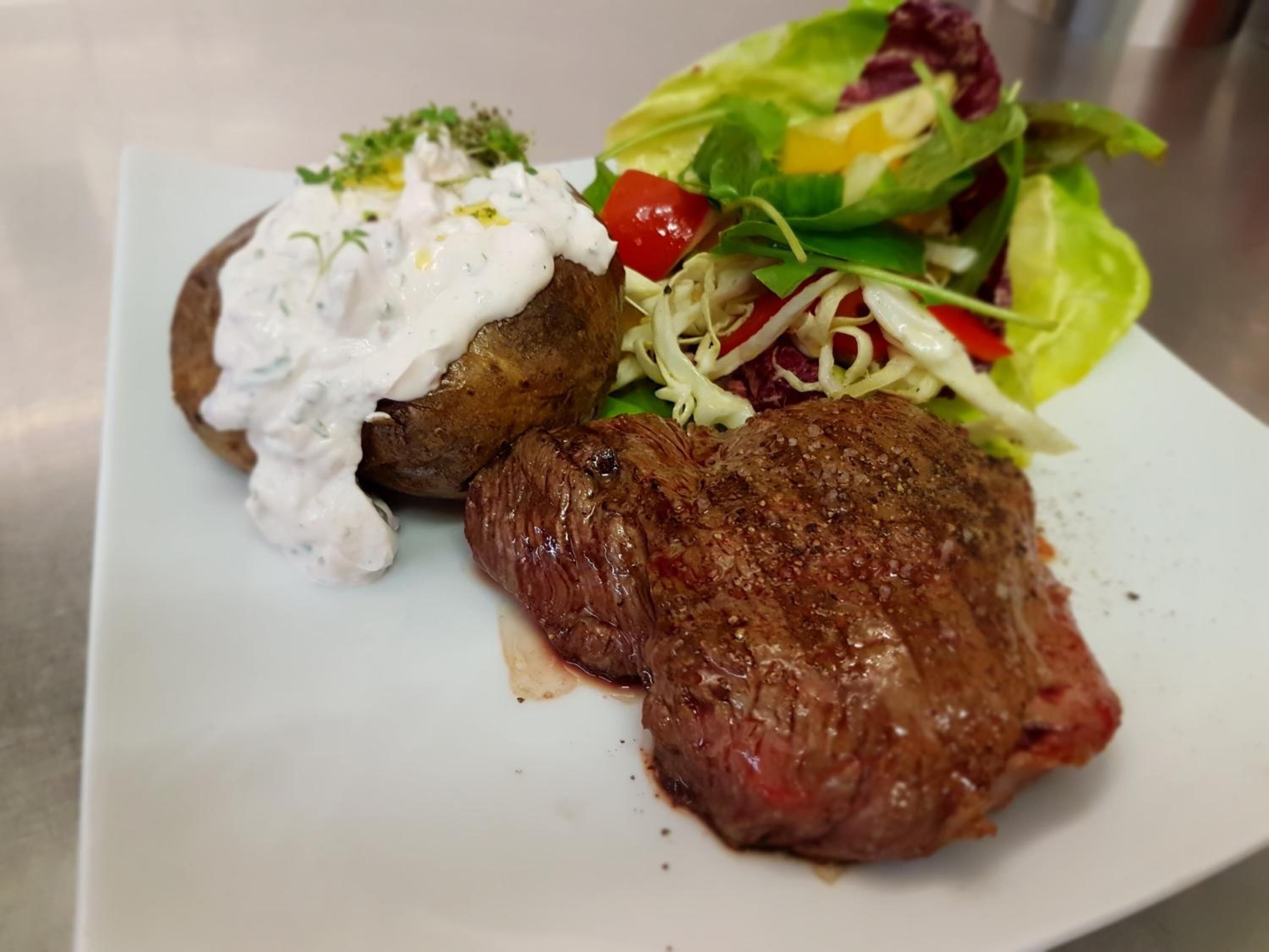 A plate with a steak, a baked potato topped with a creamy sauce, and a mixed green salad.