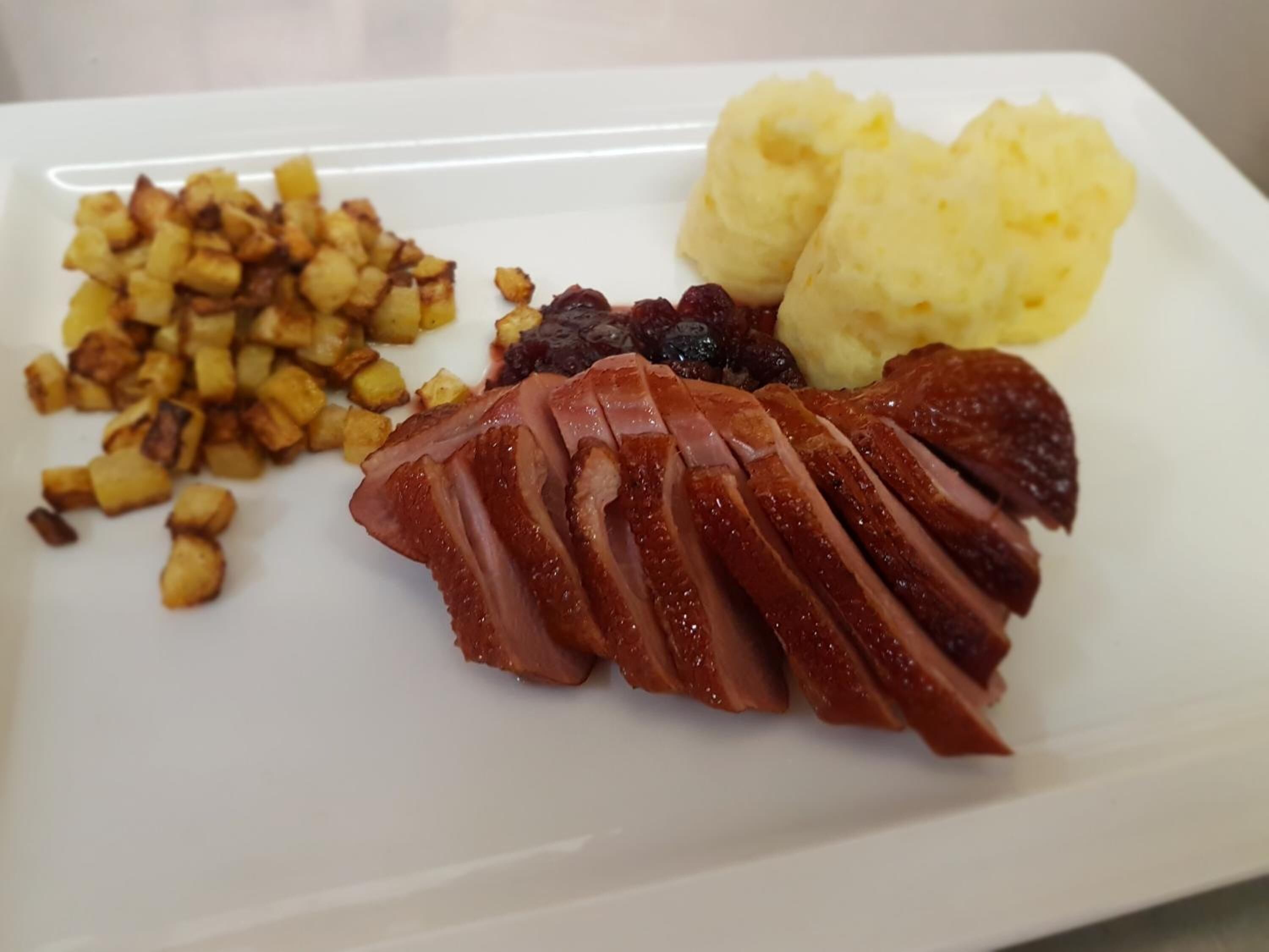 Een bord met plakjes vlees, aardappelpuree en geroosterde aardappelen.