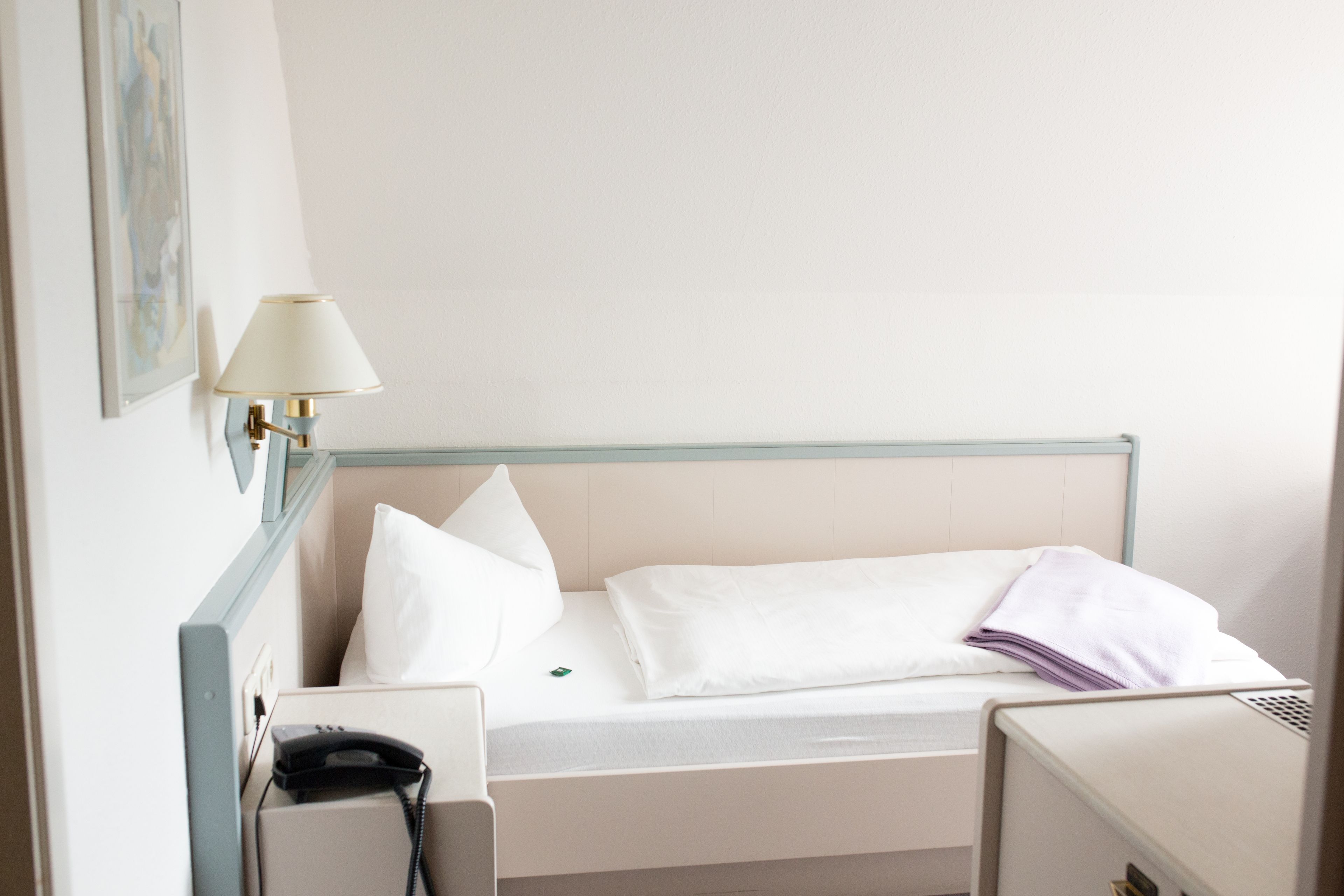 Una habitació d'hotel amb un llit individual, una làmpada de nit, un telèfon i una taula petita.