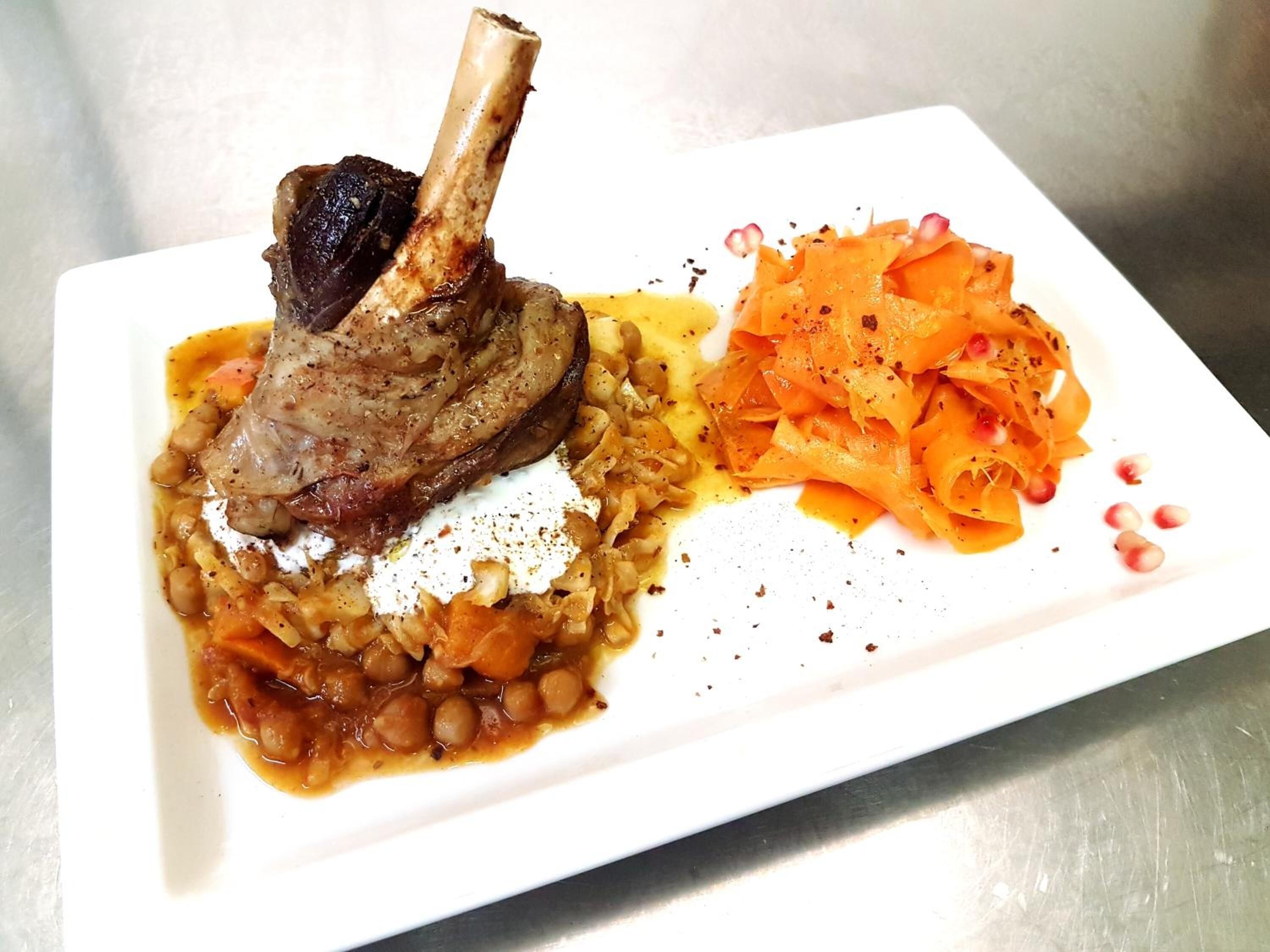 A plate with a lamb shank, beans, and a carrot salad.