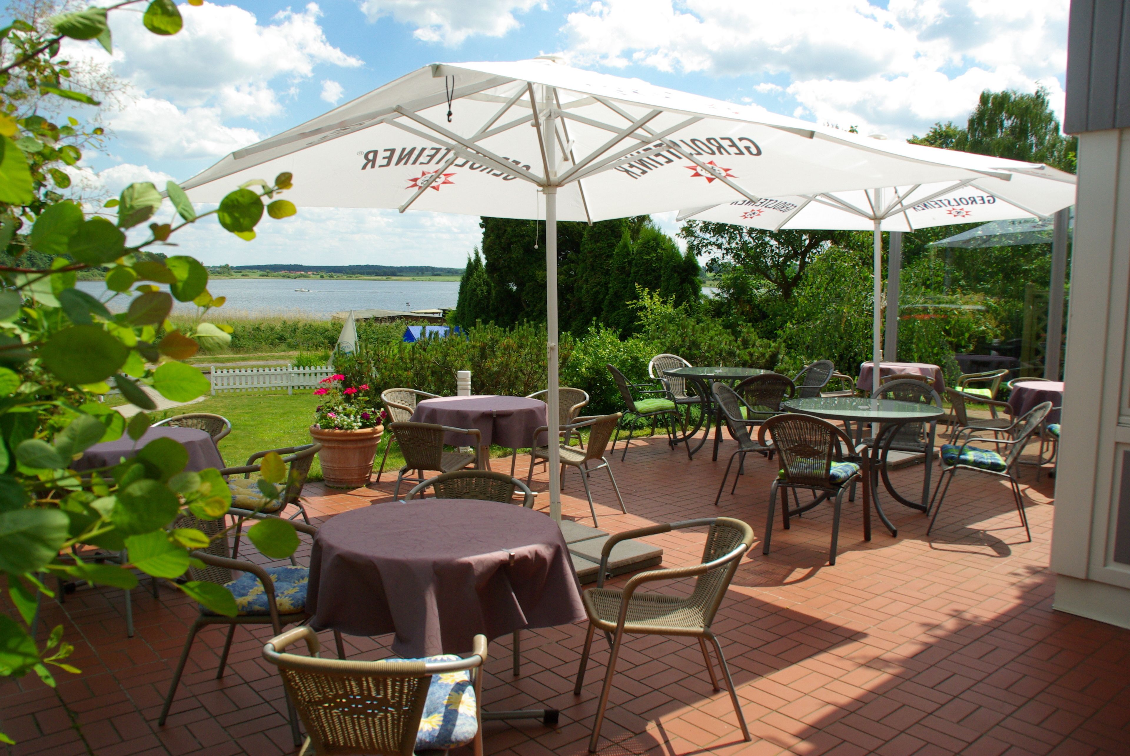 An outdoor patio with tables and chairs, umbrellas, and a view of the water.