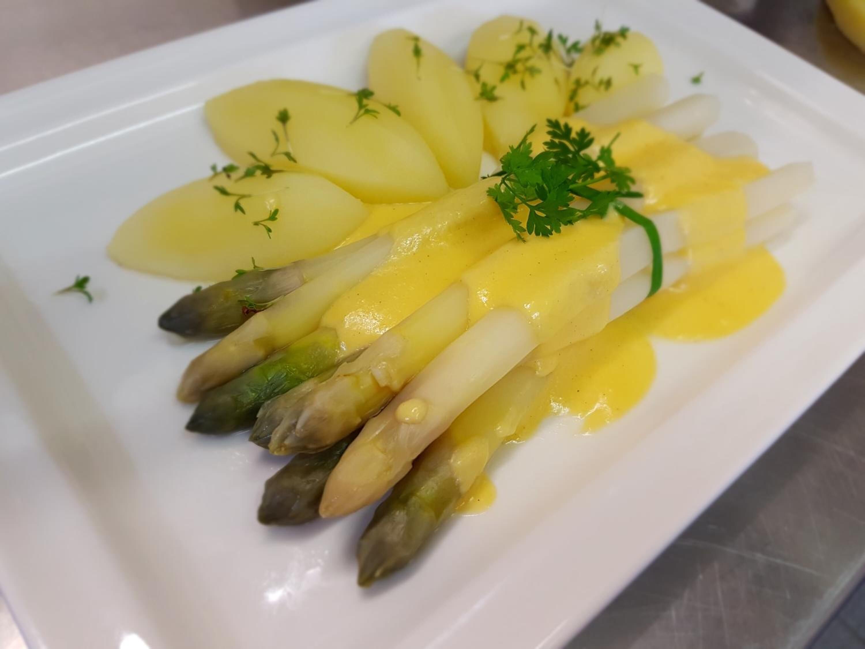 Plato blanco con patatas en rodajas y espárragos, adornado con perejil.