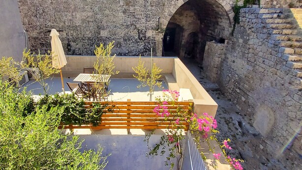 A courtyard with stone walls, a wooden bench, and a table with chairs. - Saint George Studios (Rhodes)
