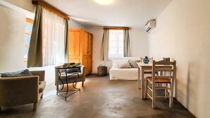 A compact living space with a sofa, a dining table with chairs, a small kitchen area, and a window with curtains. - Saint George Studios (Rhodes)