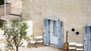 A building with a tiled roof, stone walls, and a small garden with a tree and flowers. - Masseria dei Monaci (Otranto)