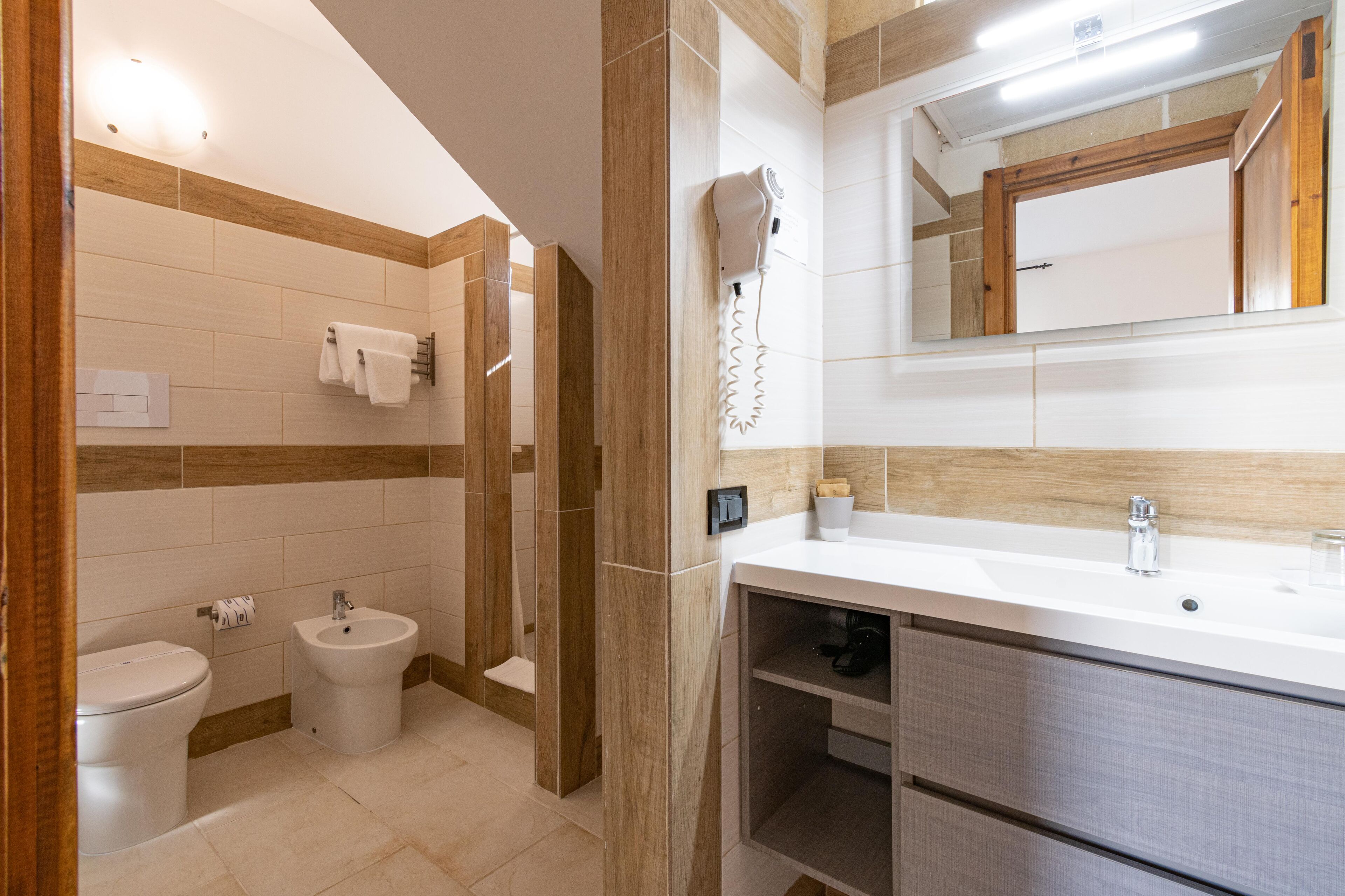 Un baño moderno con inodoro, bidé, tocador con espejo y un perchero para toallas.