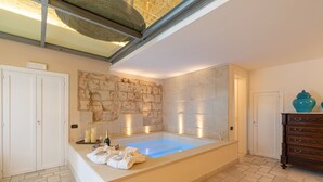 A spacious bathroom with a large bathtub, stone wall, and a wooden dresser with a blue vase. - Masseria dei Monaci (Otranto)
