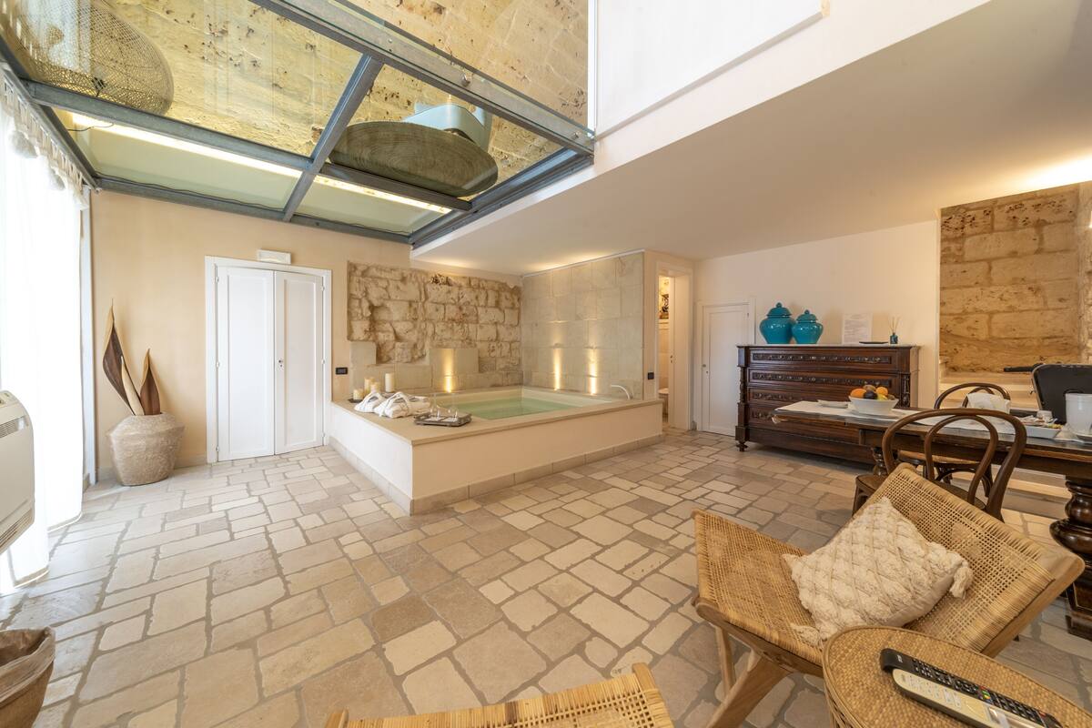 Un vaste espace de vie doté d’une grande baignoire, de murs en pierre et d’un plafond haut avec une verrière.