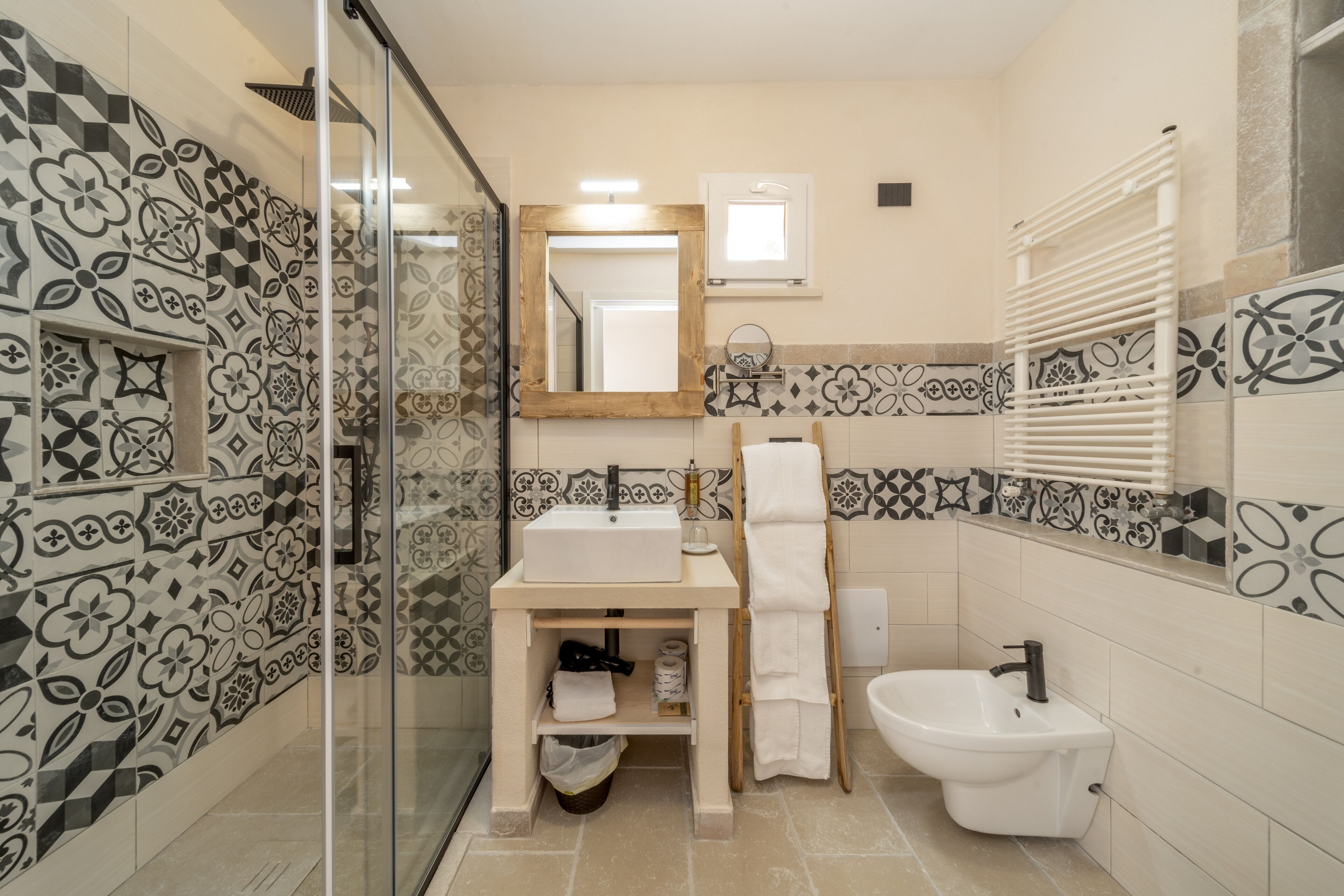 Un baño con cabina de ducha de vidrio, lavamanos con espejo, un bidé y baldosas con diseño.