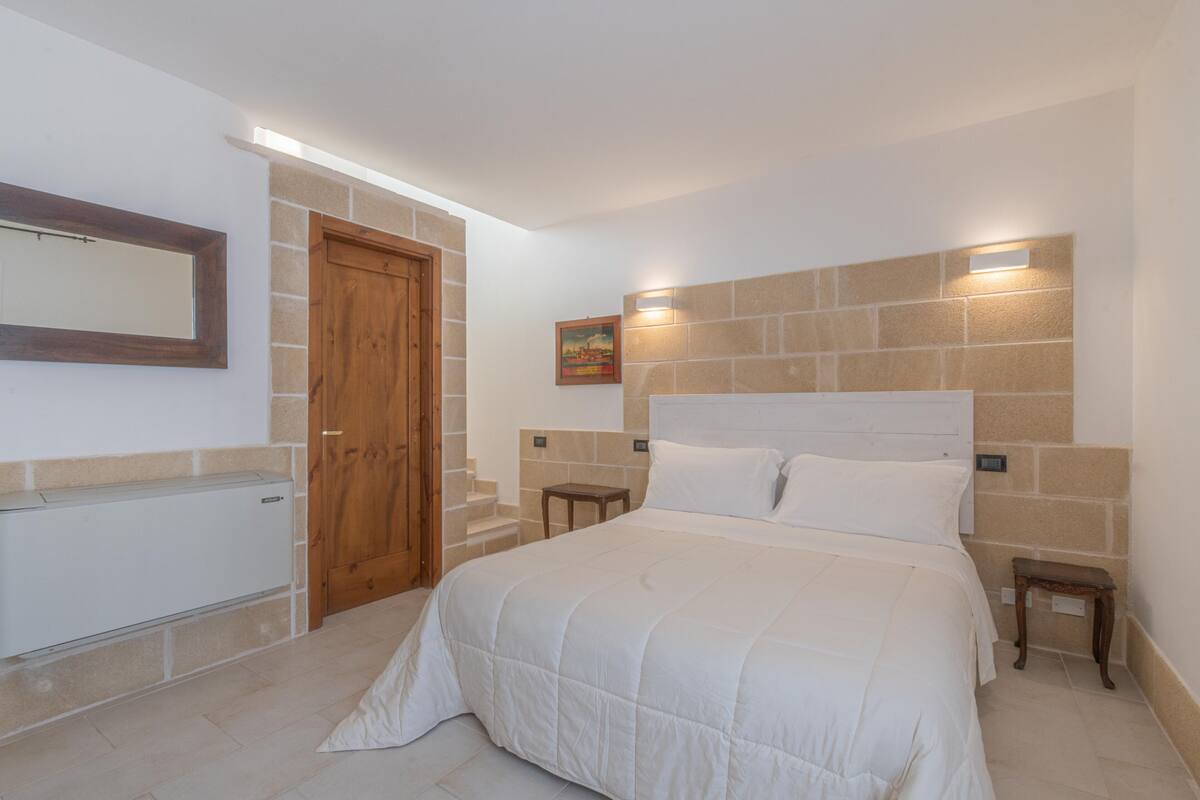 Une chambre à coucher avec un grand lit, une porte en bois, une petite table et un luminaire fixé au mur.