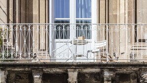 A building facade with a classical architectural style, featuring a large arched window with blue curtains, a decorative balcony railing, and intricate stone carvings. - Nostos rooms & Apartments (Syracuse)