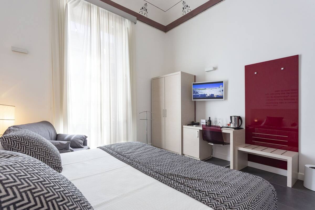 A hotel room with a bed, a desk, a chair, a television, and a red wall with text.