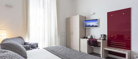 Habitación de hotel con cama, escritorio, silla, televisión y pared roja con texto.