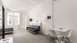 A modern, minimalist room with a sofa, a small table, and a desk with chairs. - Nostos rooms & Apartments (Syracuse)