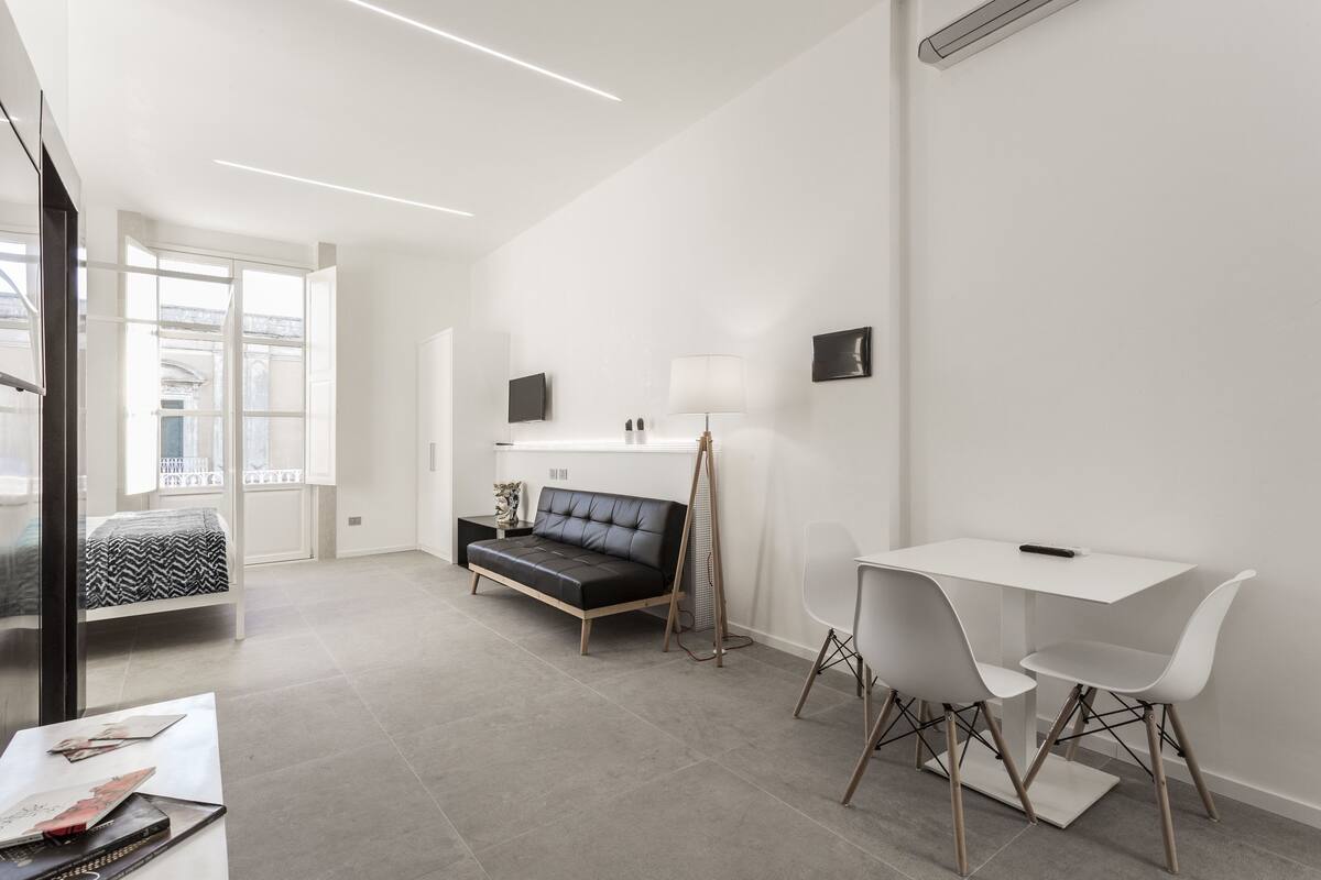 A modern, minimalist room with a sofa, a small table, and a desk with chairs.