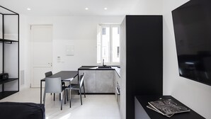 A modern kitchen with a dining area, a black TV on a stand, and a door leading to another room. - Nostos rooms & Apartments (Syracuse)