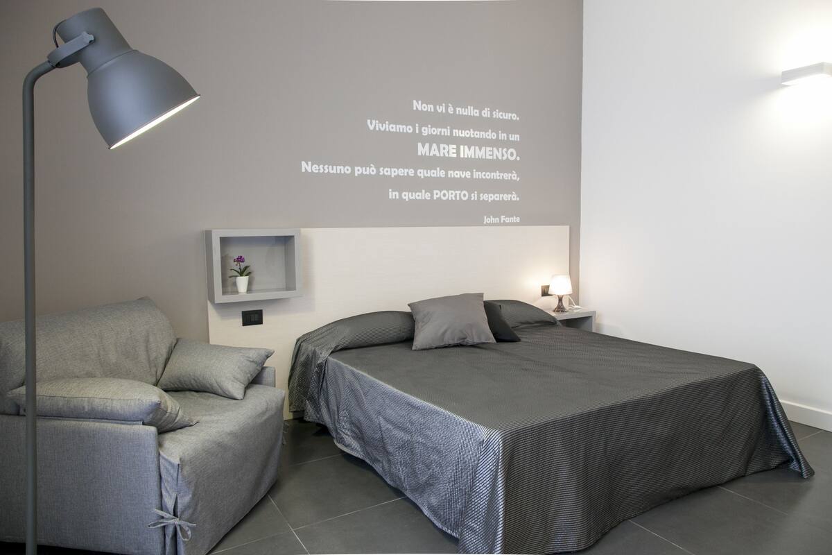 A modern bedroom with a bed, a sofa, a desk, and a wall-mounted shelf.