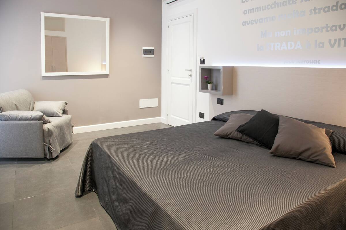 A modern bedroom with a large bed, a sofa, and a mirror on the wall.
