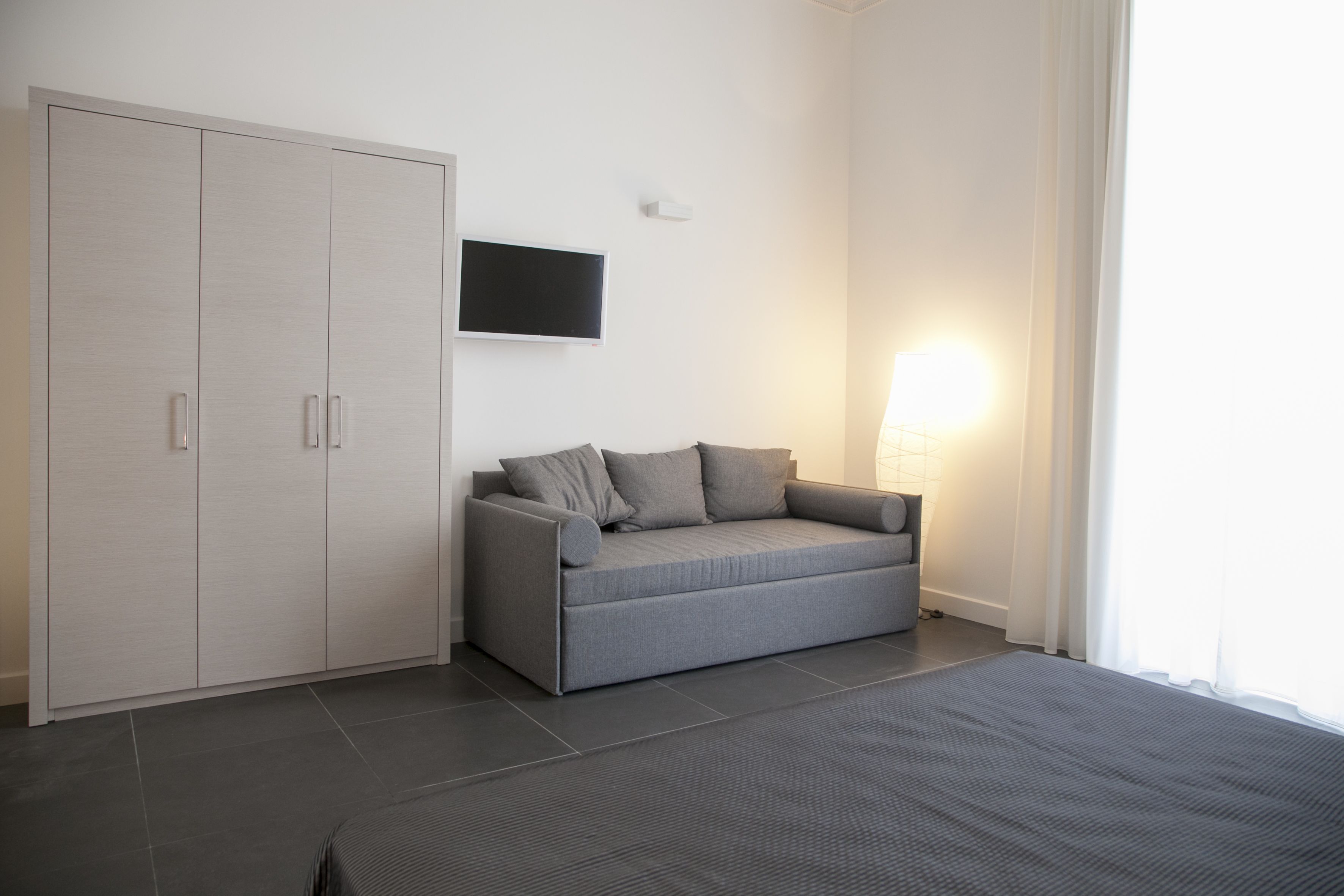 Quarto moderno com sofá cinza, guarda-roupa e televisão de ecrã plano fixada na parede.