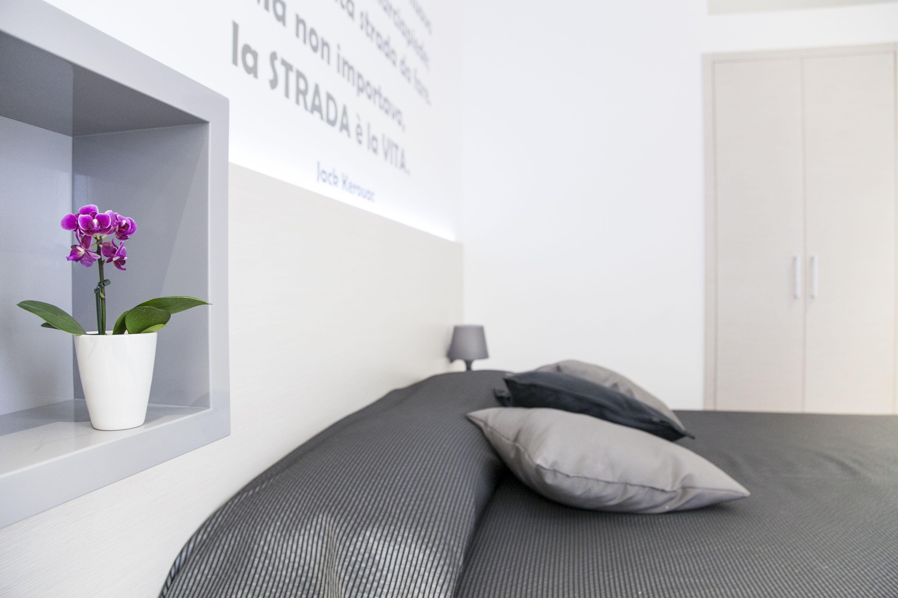 A modern bedroom with a bed, a potted orchid, a wall-mounted shelf, and a wardrobe.