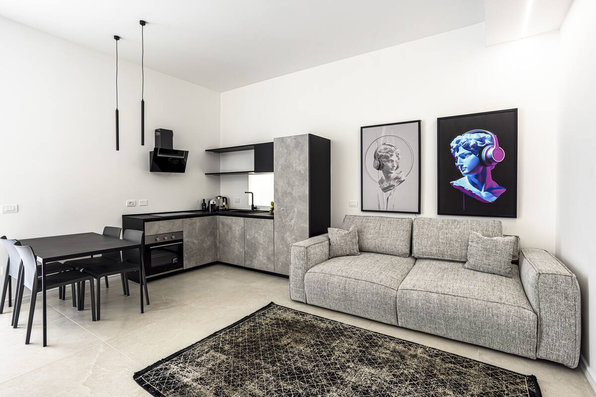A modern kitchen with a dining area, a gray sofa, and two framed artworks on the wall.