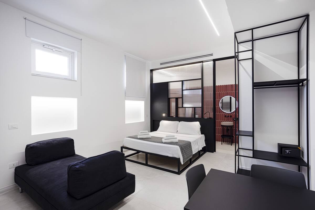 A modern hotel room with a bed, a desk, a chair, and a sofa.