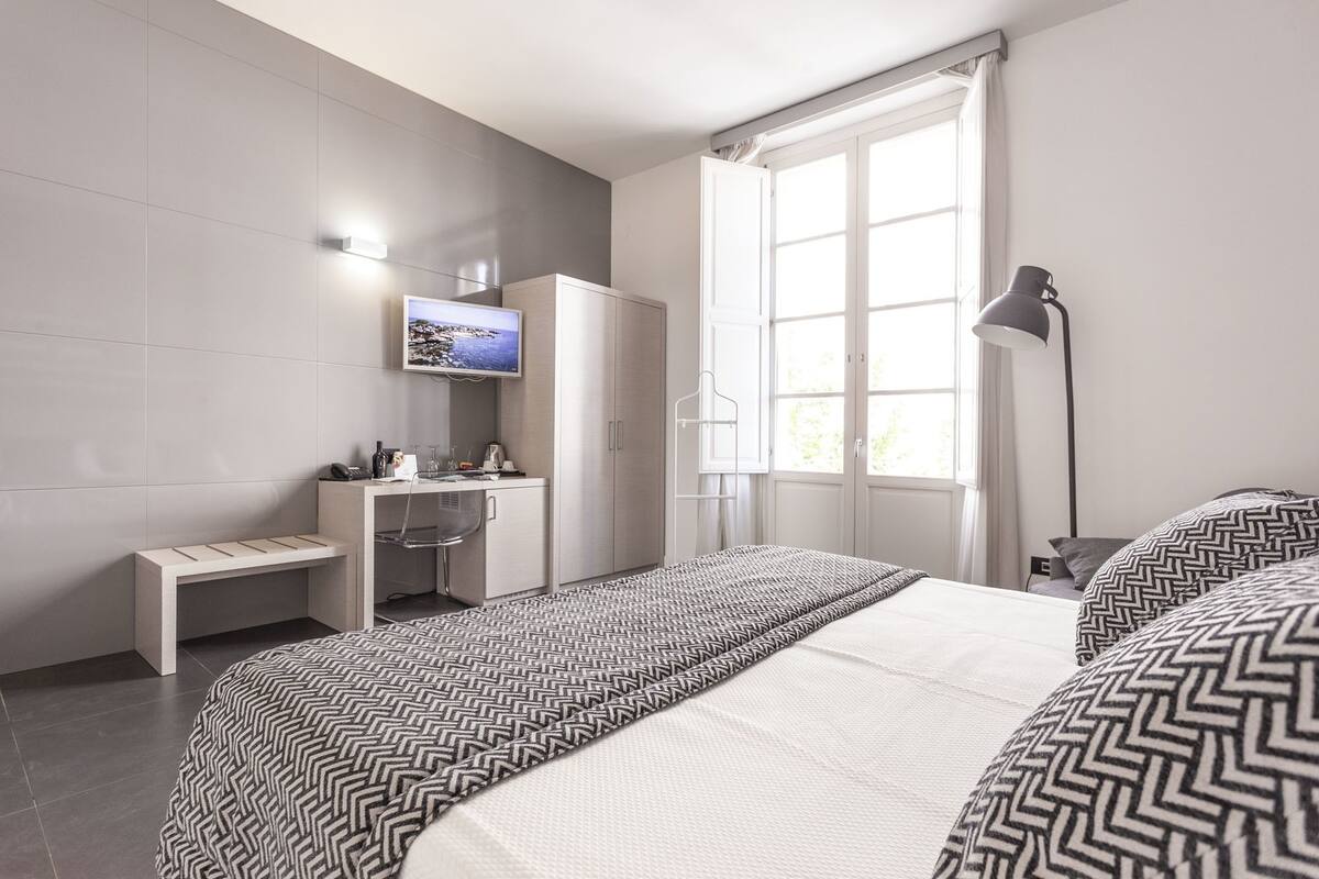 A modern hotel room with a bed, a desk, a television, and a window with curtains.