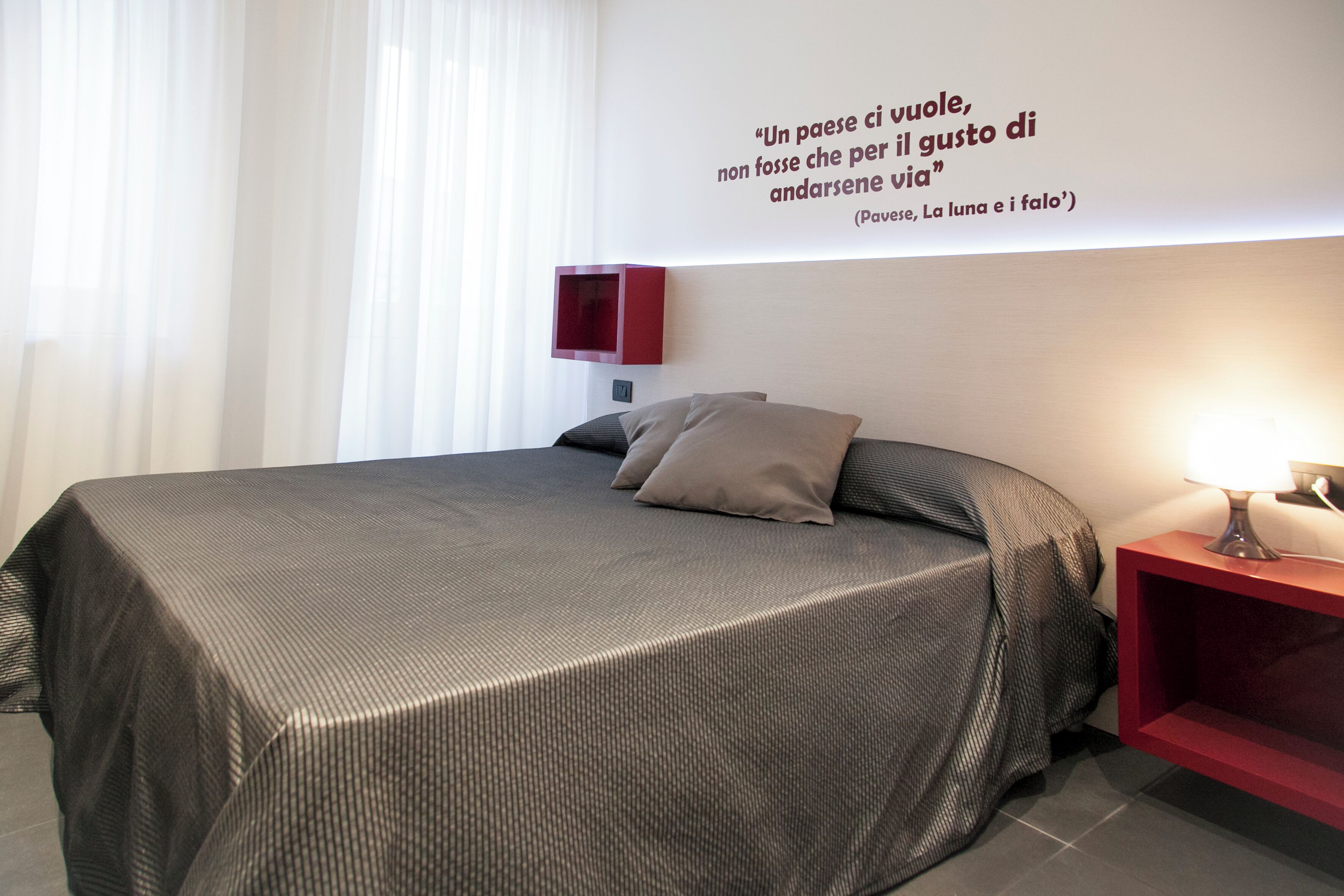 Une chambre à coucher moderne avec un grand lit, une table de chevet avec une lampe et une citation affichée sur le mur.
