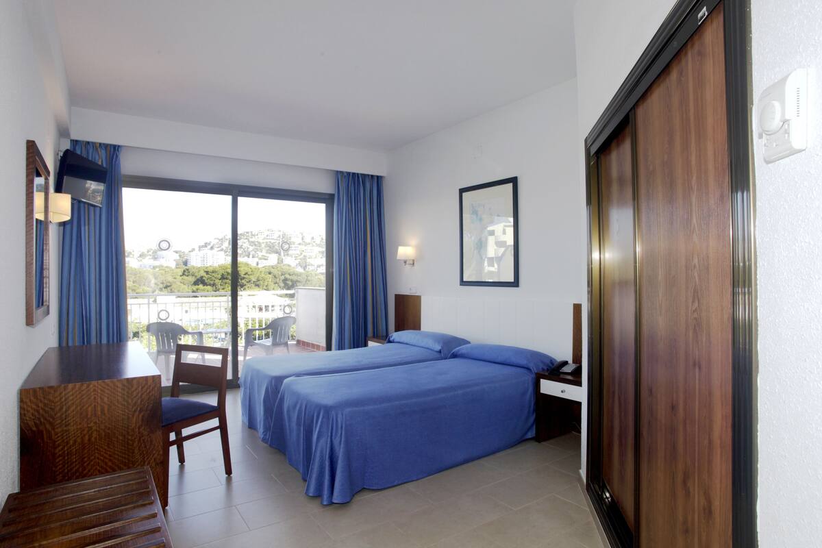 Een hotelkamer met twee bedden, een bureau, een stoel en uitzicht op de stad.