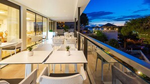 A modern outdoor dining area with glass walls, white furniture, and a view of a mountain at dusk. -  Hotel Casablanca Mallorca (Calvia)