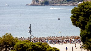 A beach with umbrellas and sun loungers, a view of the sea, and buildings in the background. -  Hotel Casablanca Mallorca (Calvia)