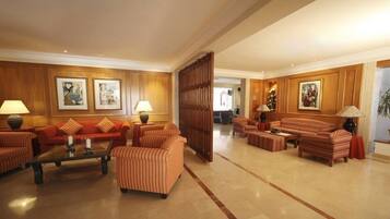 A spacious lobby with a red sofa set, striped armchairs, and a coffee table. There are framed artworks on the walls and a wooden partition.
