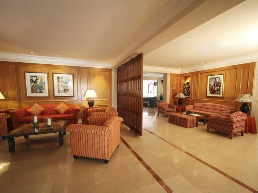 Un vestíbulo amplio con un sofá rojo, sillones a rayas y una mesa de centro. Se observan obras de arte enmarcadas en las paredes y un panel de madera.