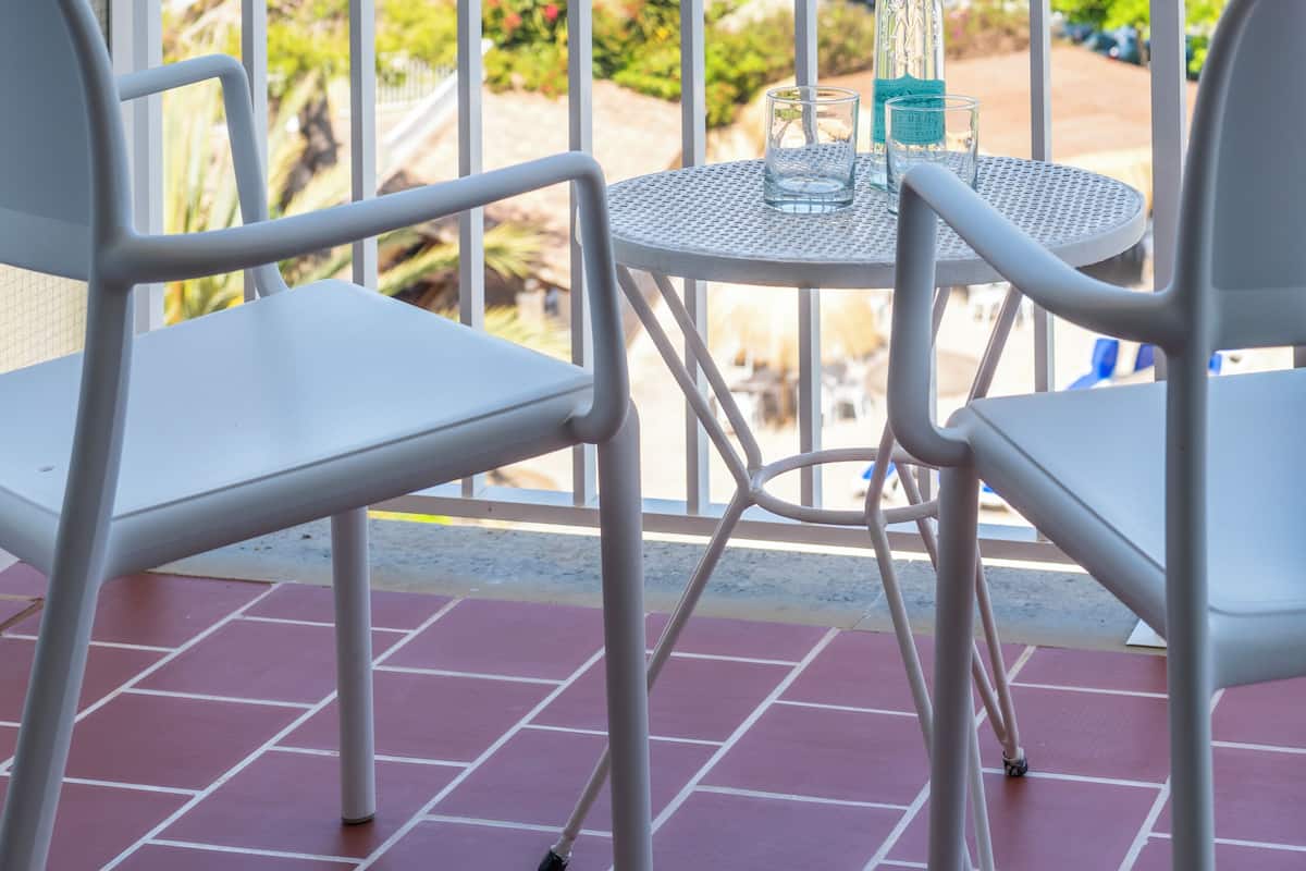 Een balkon met twee witte stoelen en een tafel, met uitzicht op een prachtig zeegezicht en groen.