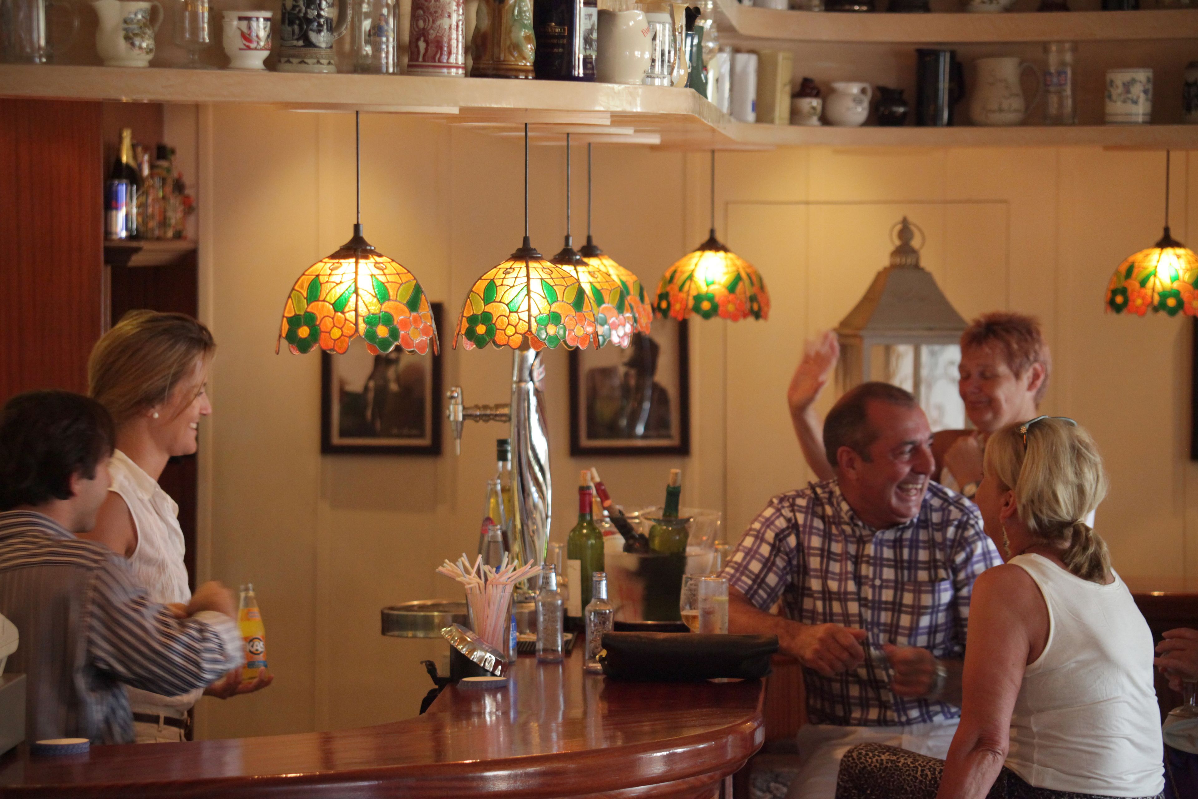 A bar area with multiple hanging lamps, a counter with various bottles, and a shelf with kitchenware.