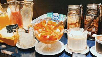 A breakfast buffet with various food and drink options, including a bowl of fruit, a glass of milk, and several jars of cookies.