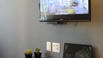 Una habitación moderna con un televisor de pantalla plana montado en la pared, un ordenador portátil sobre un escritorio y dos plantas en macetas.
