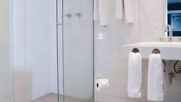 Un baño moderno con cabina de ducha de vidrio, un lavamanos blanco y dos toallas colgadas en la pared.