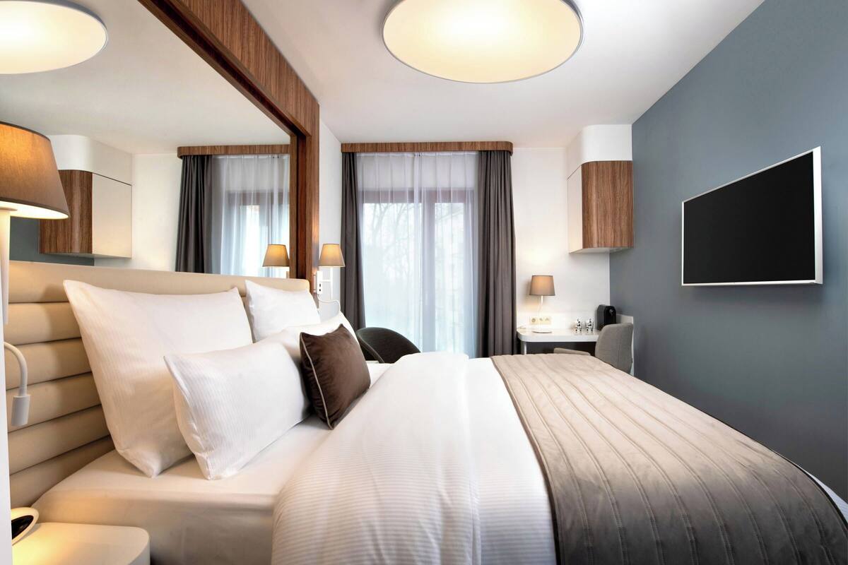 A hotel room with a large bed, bedside tables, a desk, and a TV.