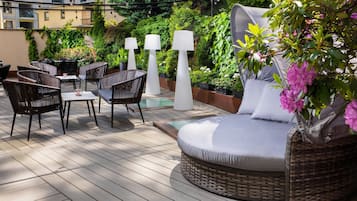 Un patio al aire libre con mobiliario de mimbre, una zona de estar acolchada y plantas en macetas.