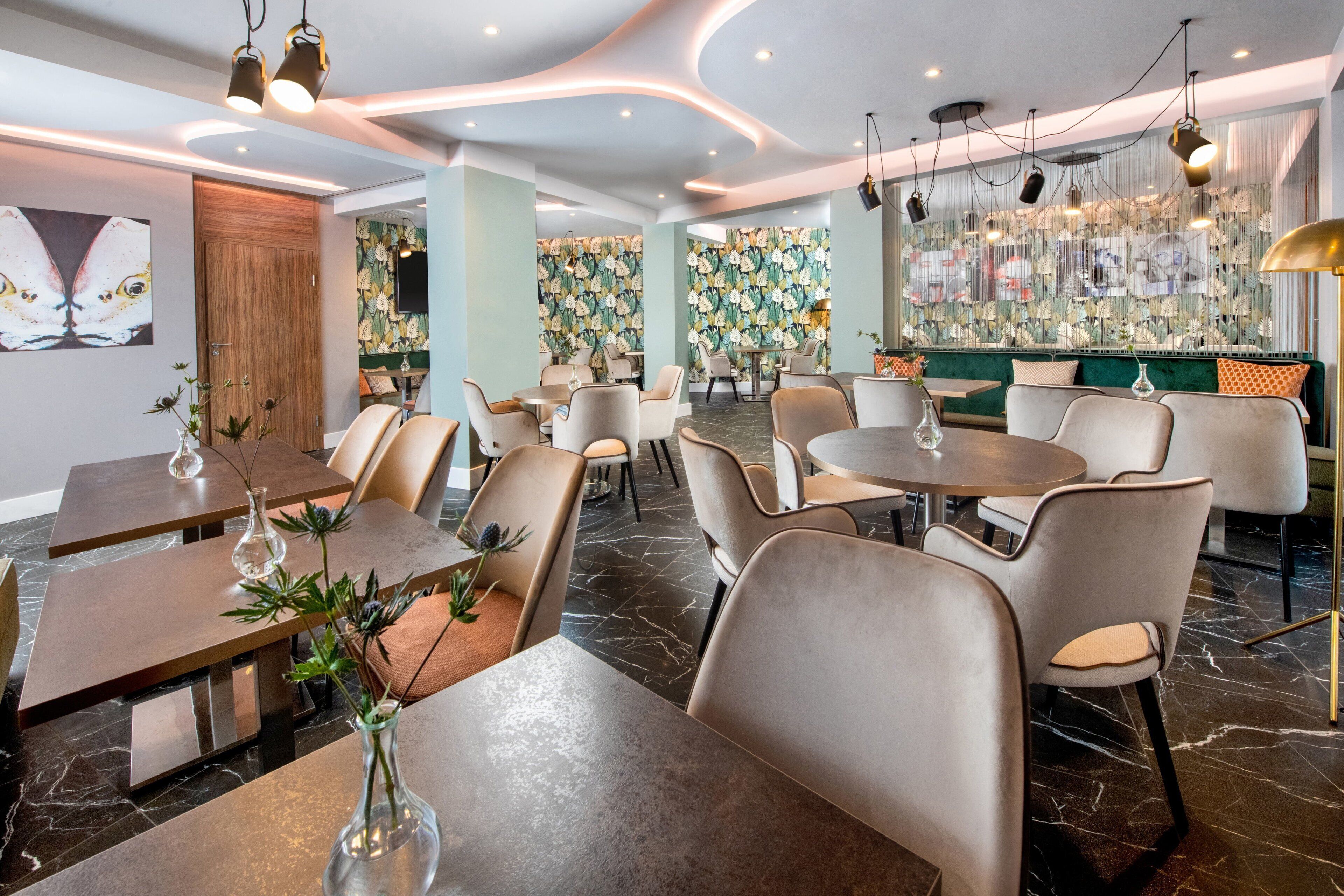Un comedor moderno con mesas redondas y sillas acolchadas, una puerta de madera y un papel tapiz con motivos florales.