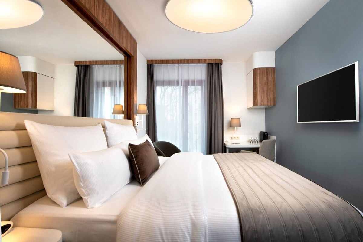 Ein modernes Hotelzimmer mit einem großen Bett, Nachttischen, einem Schreibtisch und einem Fernseher.