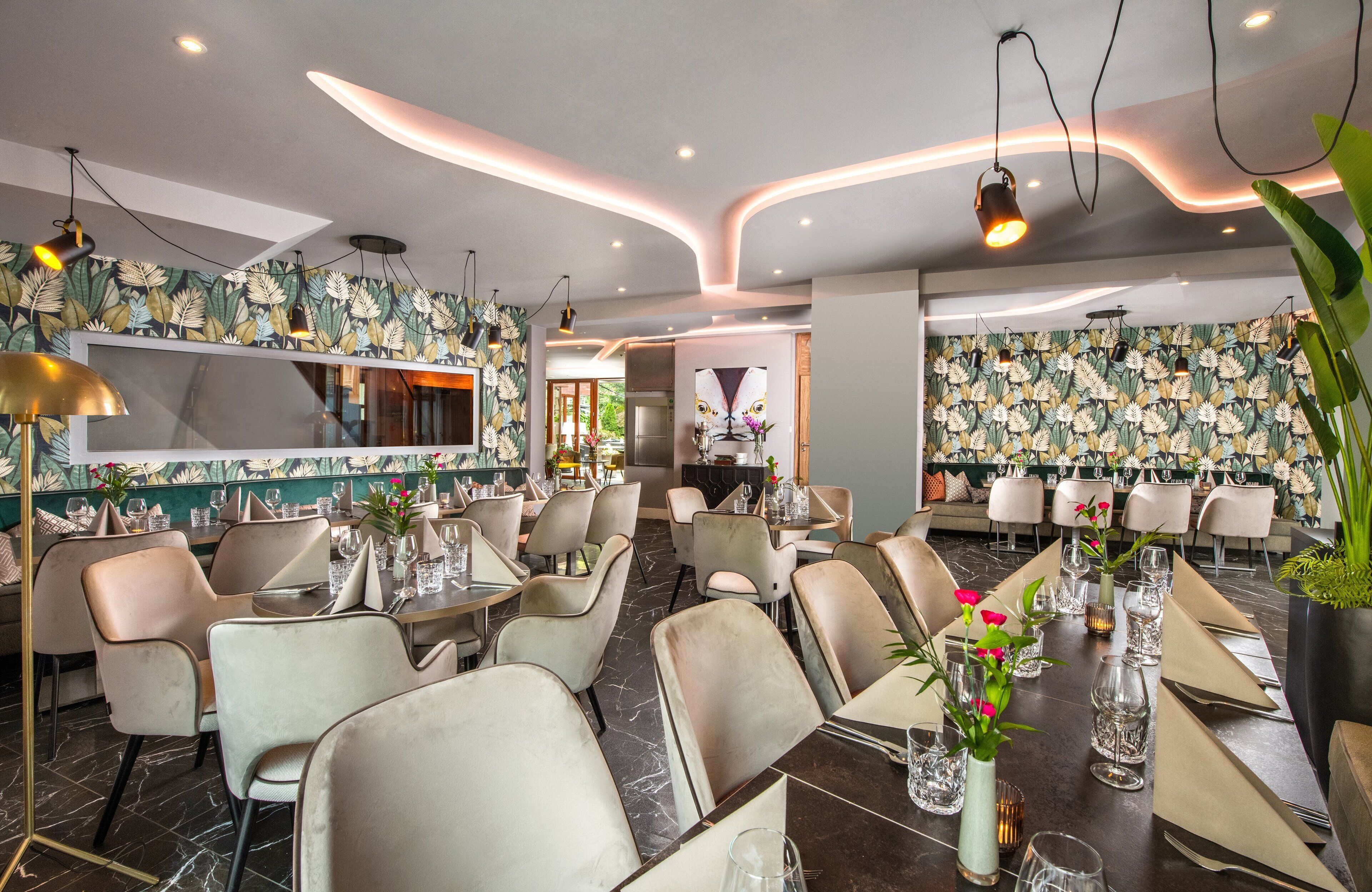 A restaurant with a modern interior, featuring a patterned wallpaper, contemporary lighting, and a variety of seating arrangements.